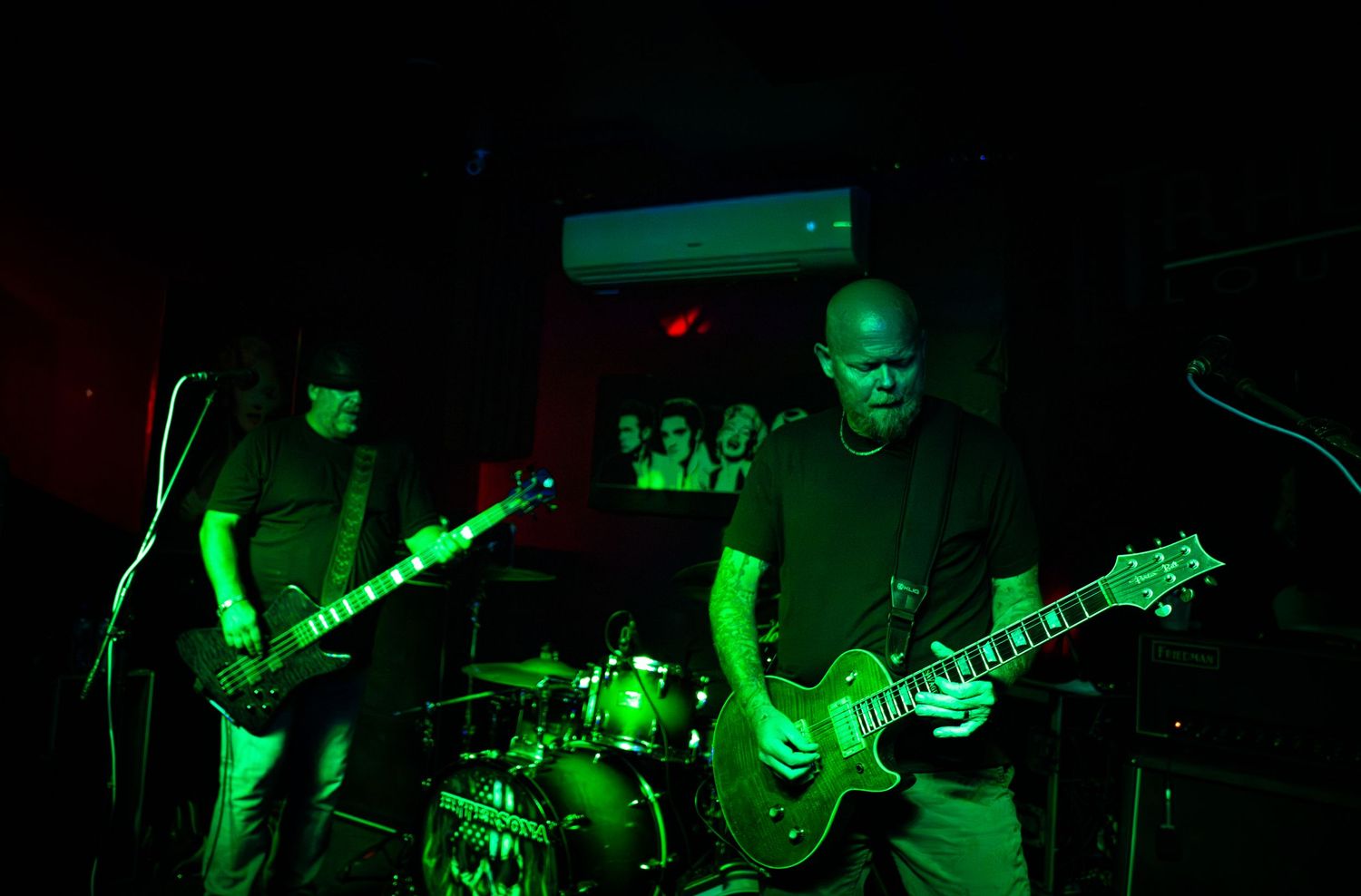 Rock band performing on stage with green lighting effects and musical equipment.