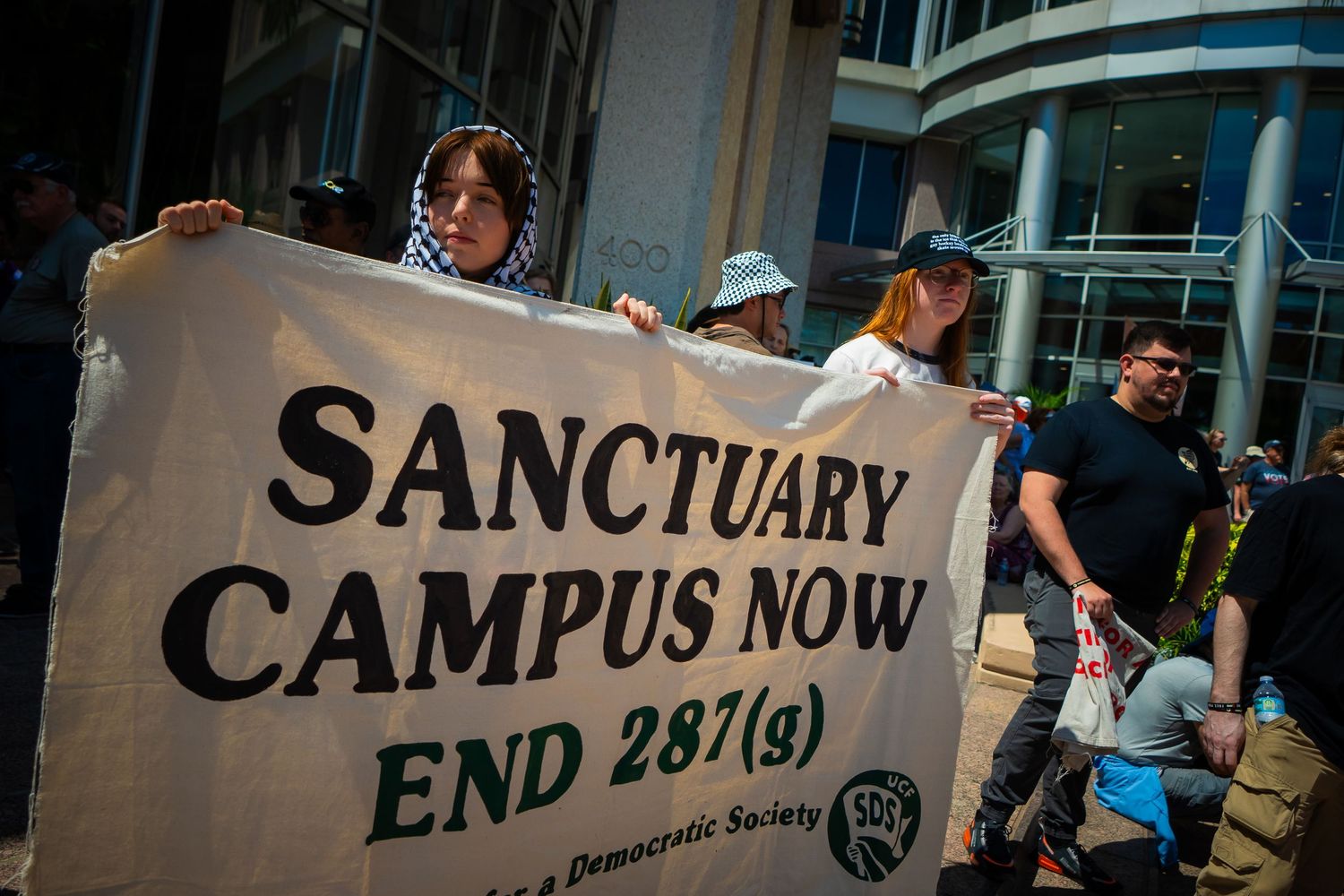 Protesters hold large white banners with text about sanctuary at a campus demonstration.