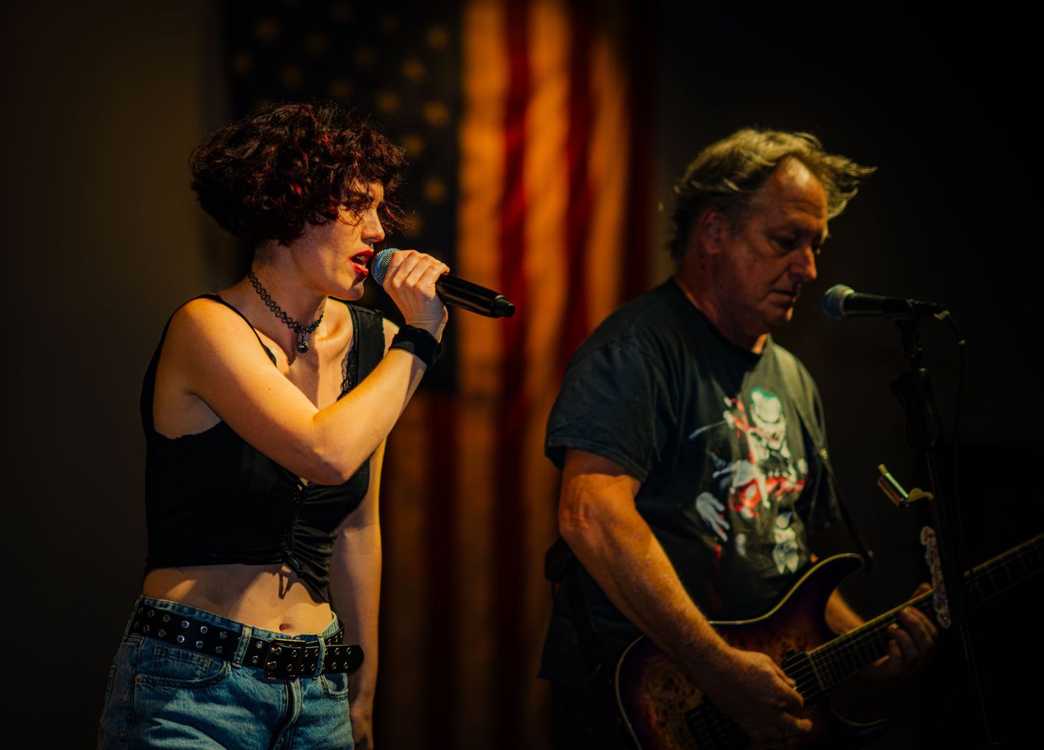 Rock band performs on stage with American flag backdrop.