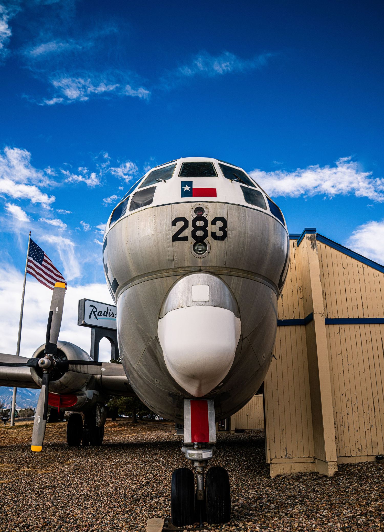 A series of vintage aircraft noses lined up in a row against blue sky and tan buildings at an aviation museum.