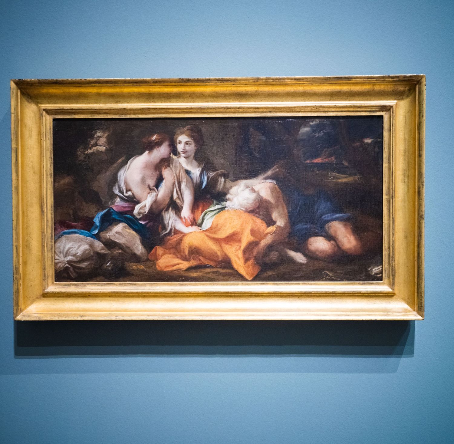 Museum gallery wall with multiple gold-framed classical paintings against blue background.