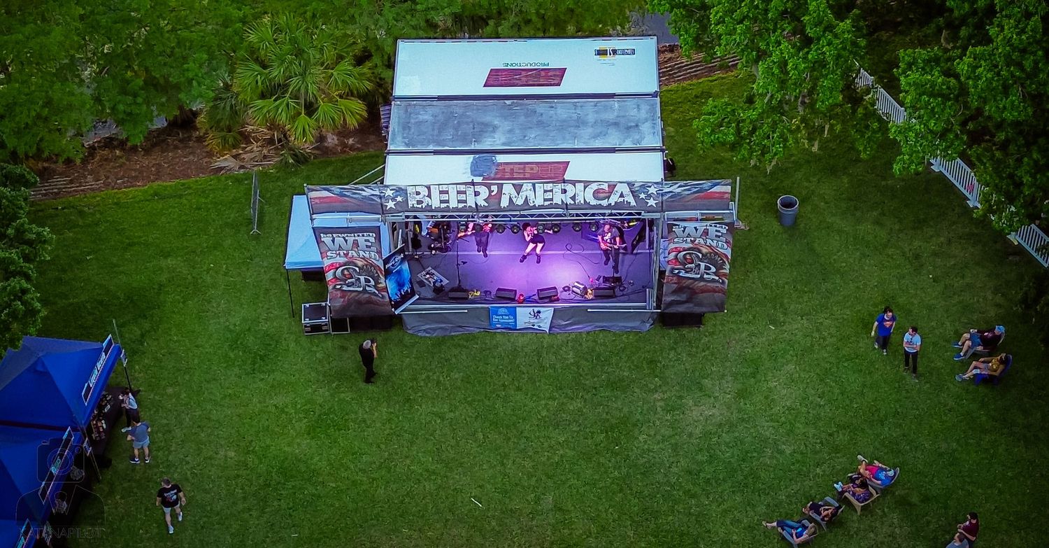 Aerial view of an outdoor event setup with tents and equipment on green grass.