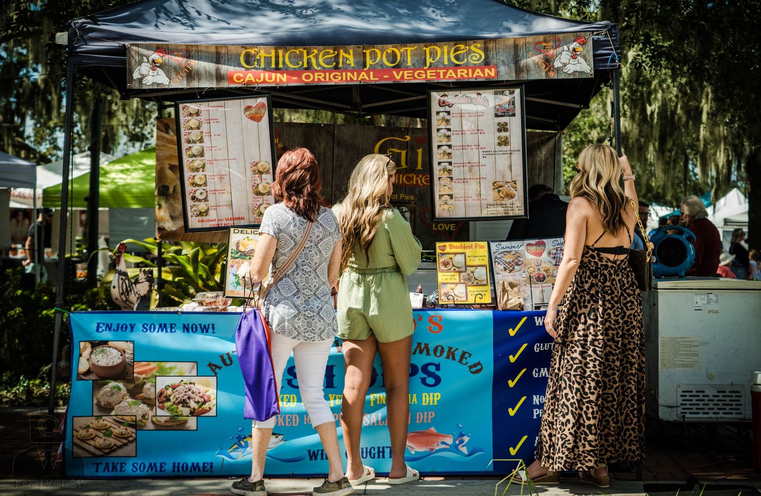 Chicken pot pie food stall with customers browsing menu at outdoor market.