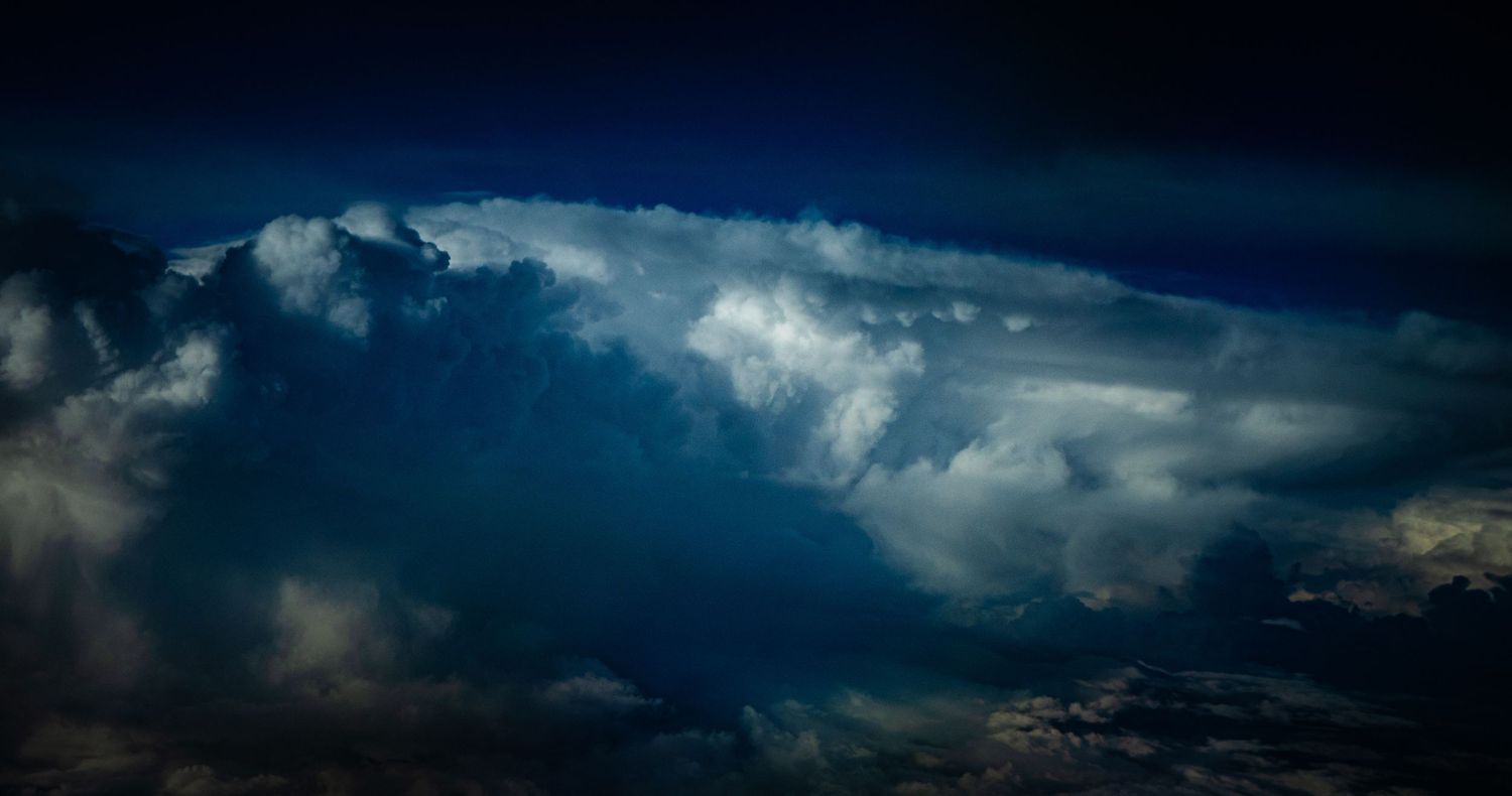 Dramatic aerial view of massive cumulonimbus storm clouds illuminated against a dark blue night sky.