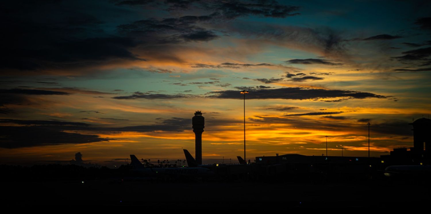 Dramatic airport sunset silhouette with vibrant orange and blue sky, control tower visible against colorful dusk horizon.