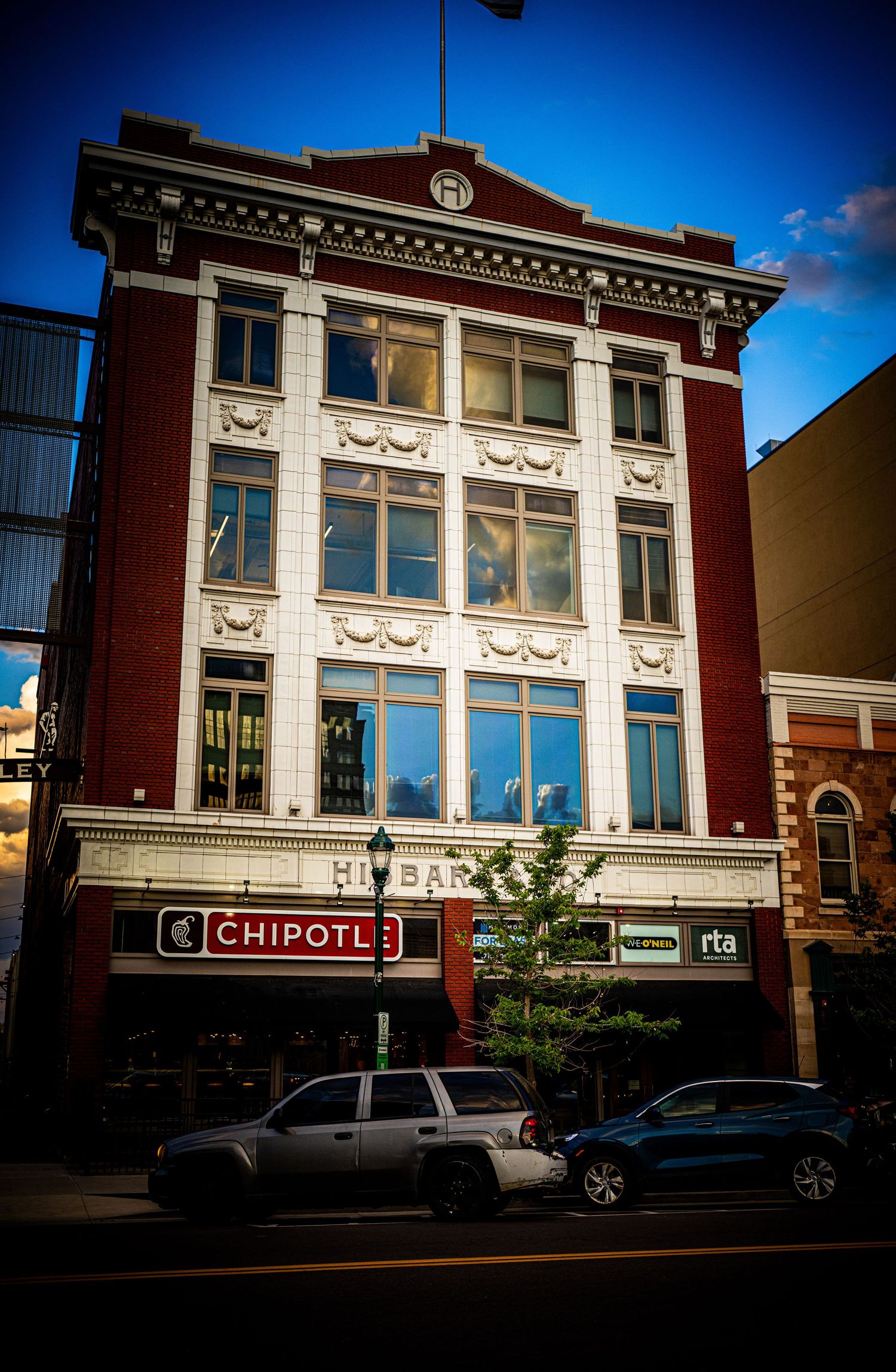 Historic red brick building housing a Chipotle restaurant on a downtown street corner with ornate white architectural details.