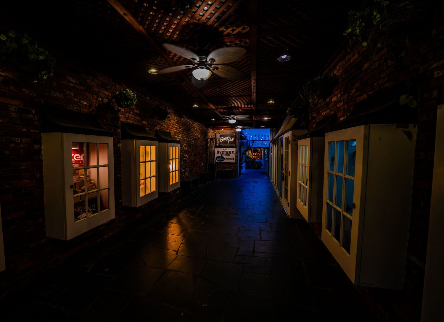 Dark corridor with warm lighting from windows and ceiling fans creating a moody atmosphere.