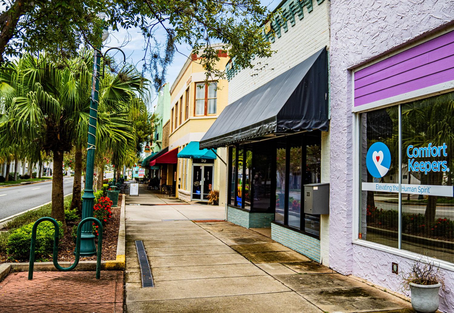 Outdoor shopping plaza walkway with palm trees and white stucco buildings.