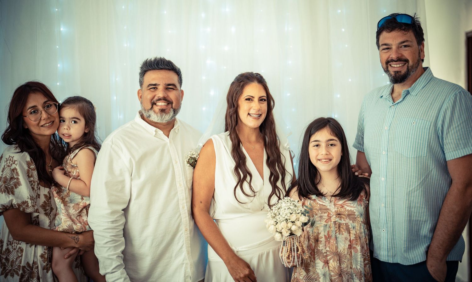 A group of people smiling and posing together against a light colored wall in a casual setting.