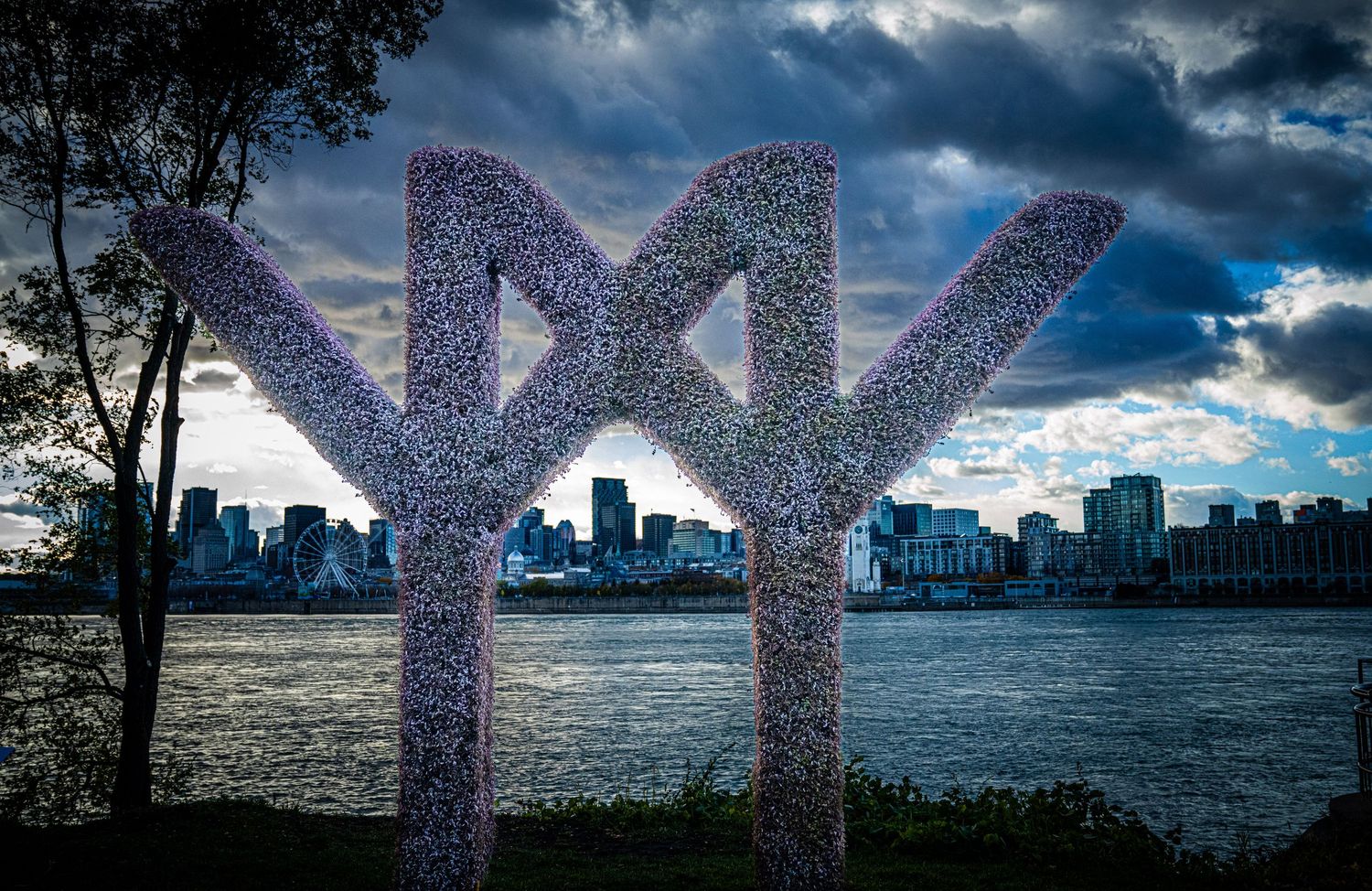 Panoramic view of large decorative letters against a dramatic cloudy sky with city skyline in the background.