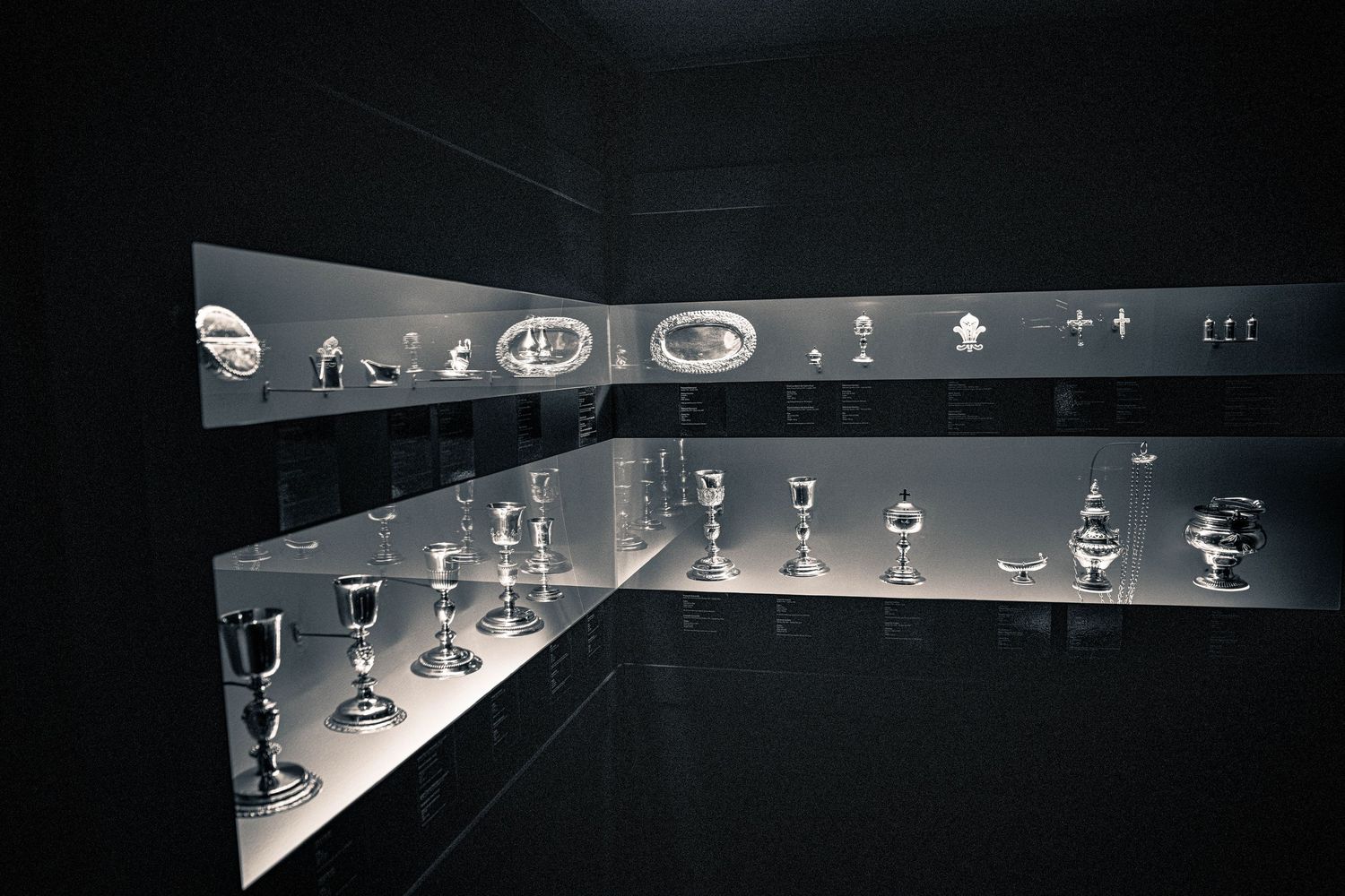 Glass display case containing antique silver objects and decorative items with dramatic lighting.