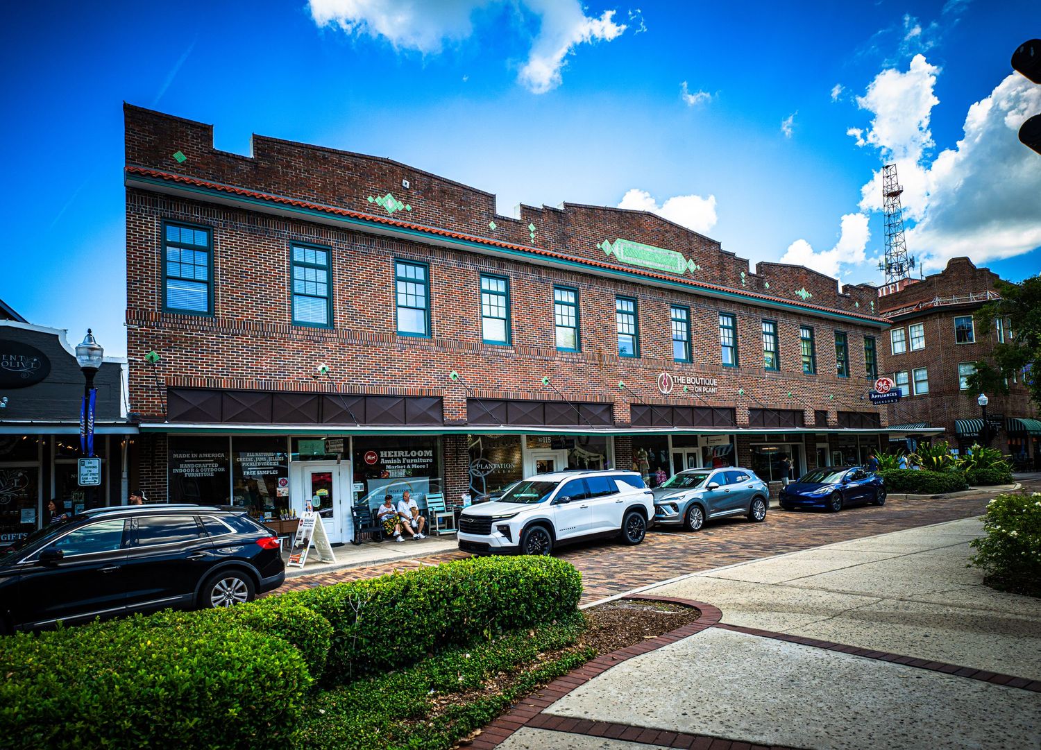 Panoramic view of a brick commercial building exterior with parked cars and landscaping.