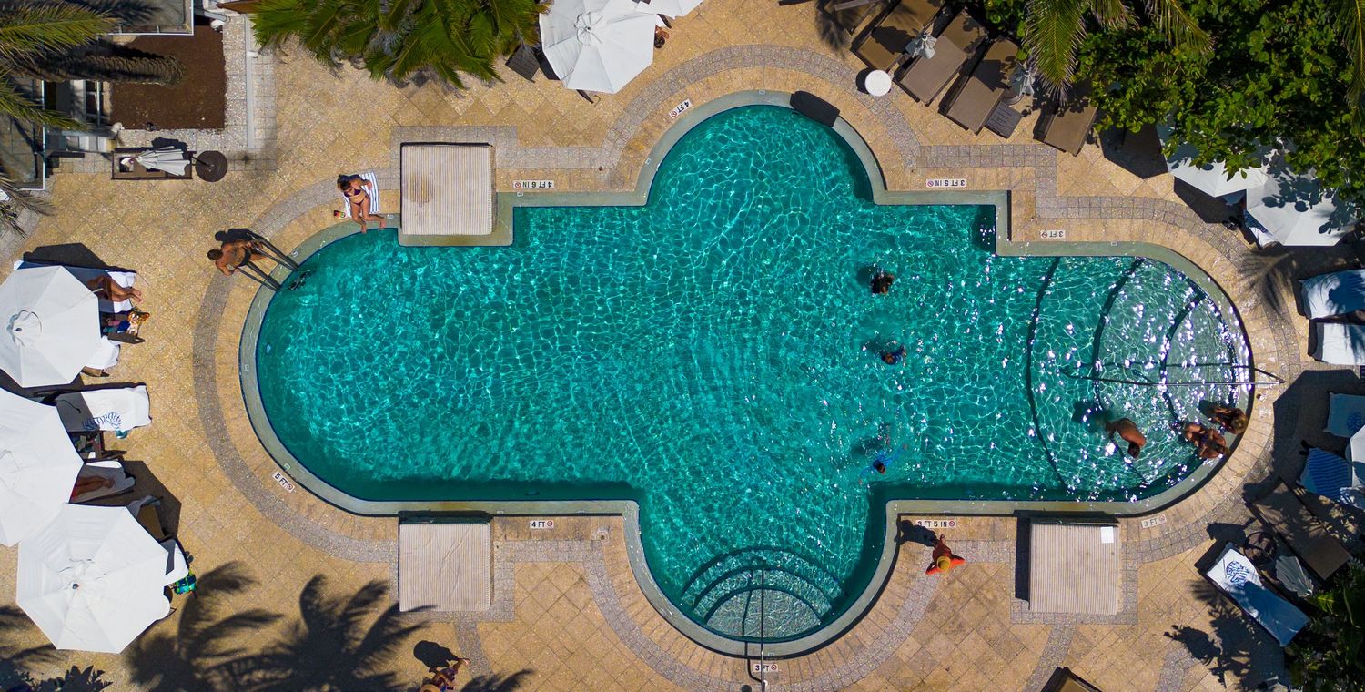 Aerial view of a uniquely shaped cross-design swimming pool with turquoise water.