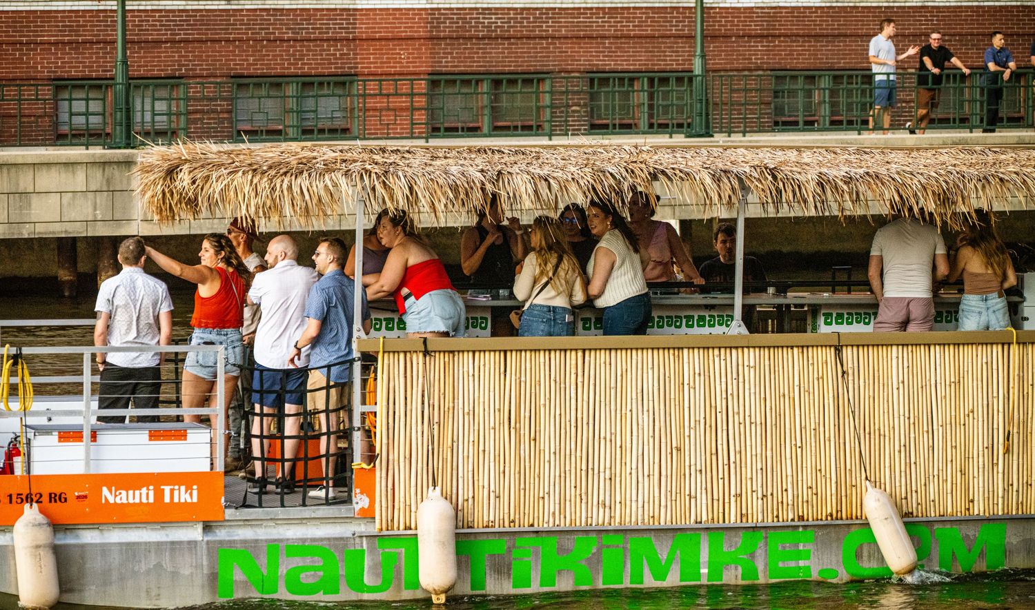 Waterfront boardwalk with tiki-style decor and green fencing along the riverbank.