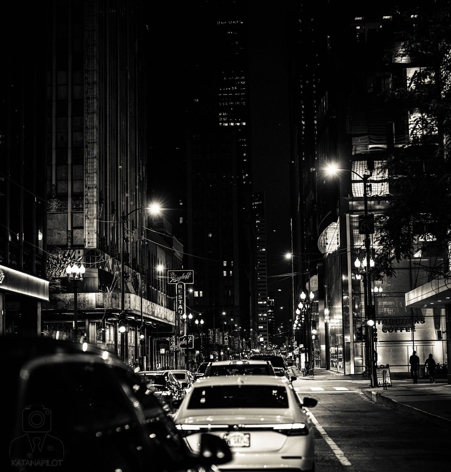 Black and white nighttime cityscape showing illuminated buildings and streets in an urban setting.