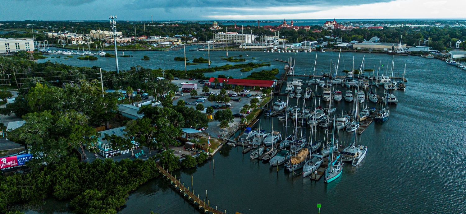 Aerial panorama of a coastal marina with boats and docks stretching across blue waters.
