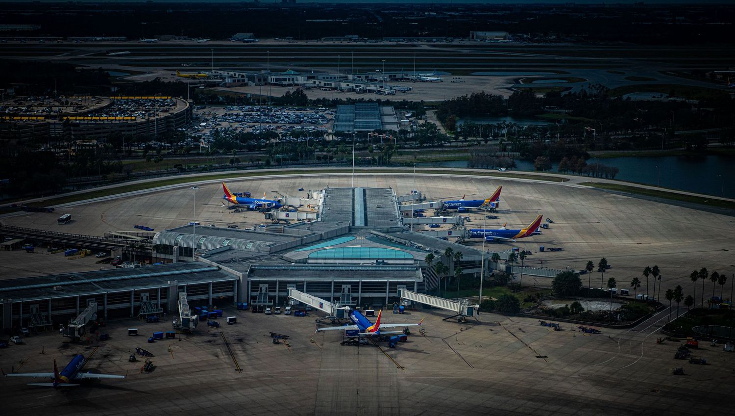Aerial view of multiple commercial airplanes parked at airport gates and terminals during sunset.