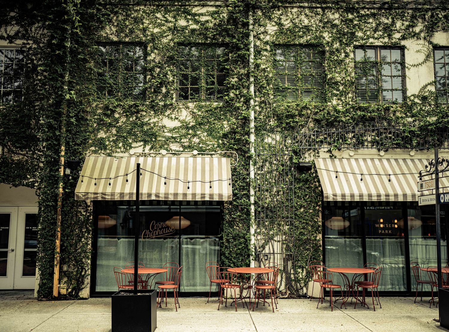 Ivy-covered brick restaurant facade with striped awnings and outdoor cafe seating on a charming urban sidewalk.