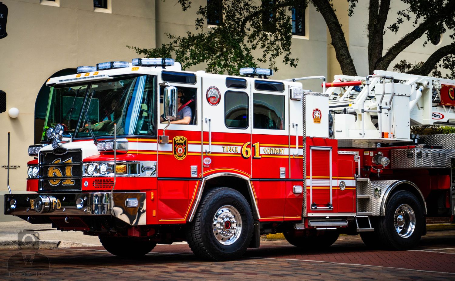 A row of red fire engines and emergency response vehicles parked on a brick paved street.