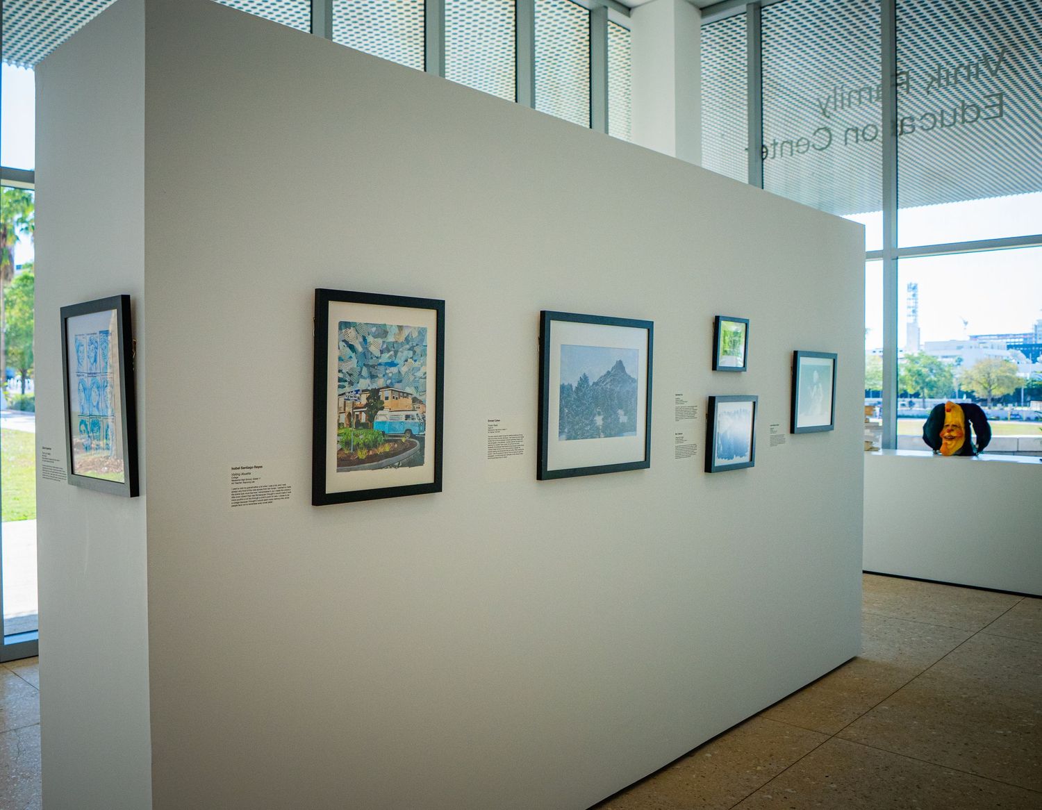 Art gallery interior with framed artwork displayed on white walls in a well-lit exhibition space.