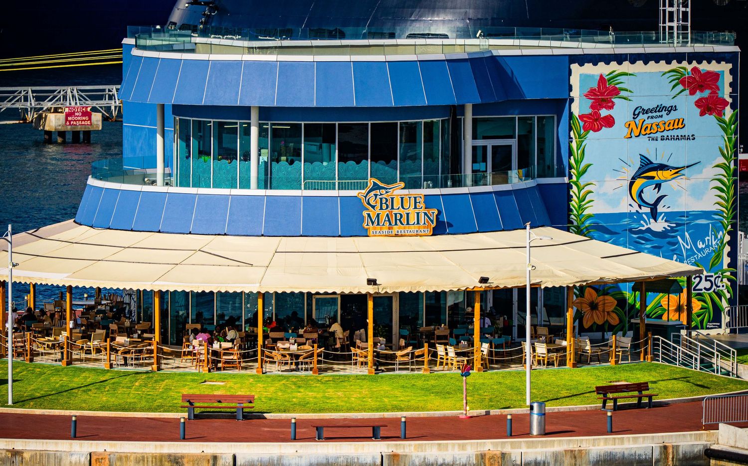 Aerial view of the Blue Marlin waterfront restaurant with outdoor seating, blue glass facade, and colorful tropical signage.