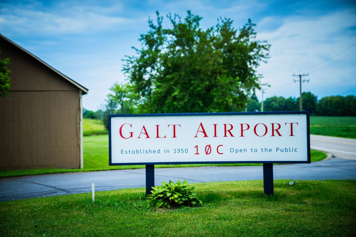 Small regional airport entrance sign surrounded by green grass and trees.