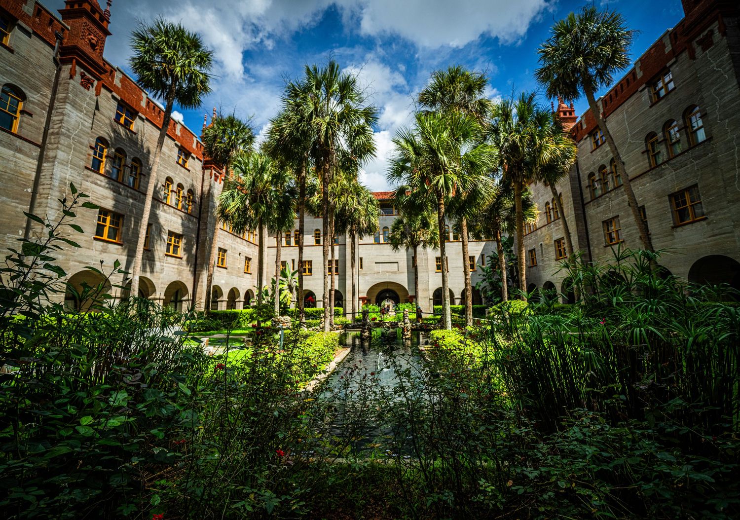 Historic Spanish colonial architecture with palm trees and arched walkways under bright blue sky.