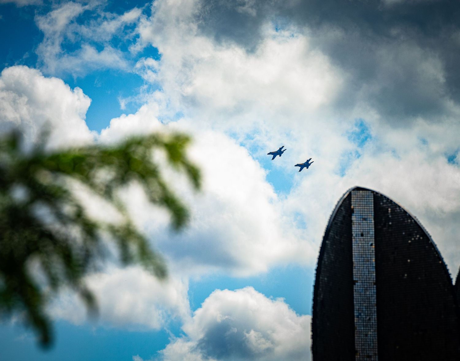 Jets perform aerial maneuvers leaving contrails across a cloudy blue sky.