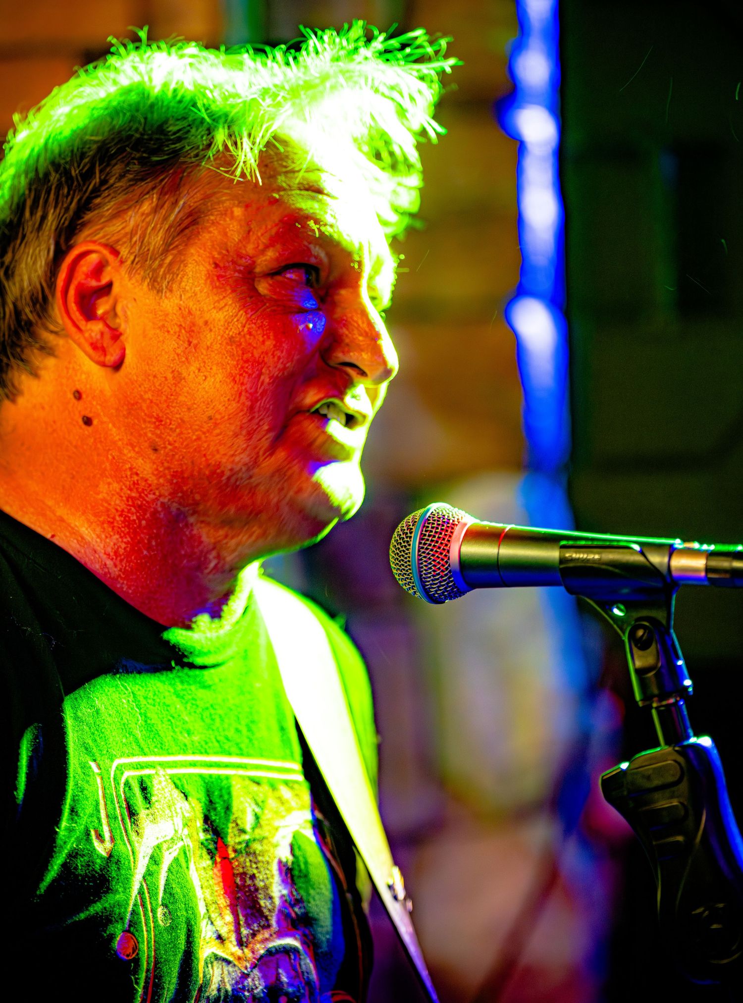 A performer singing into a microphone under bright green stage lighting during a live music performance.