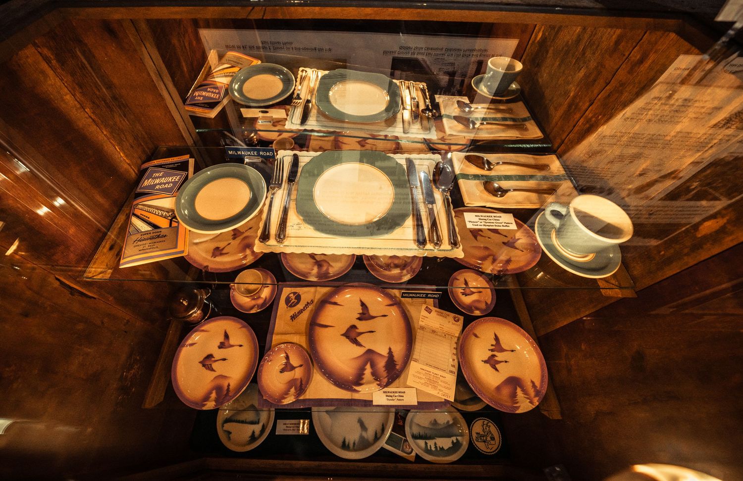 Antique dining car plates and tableware arranged in illuminated museum display cases.