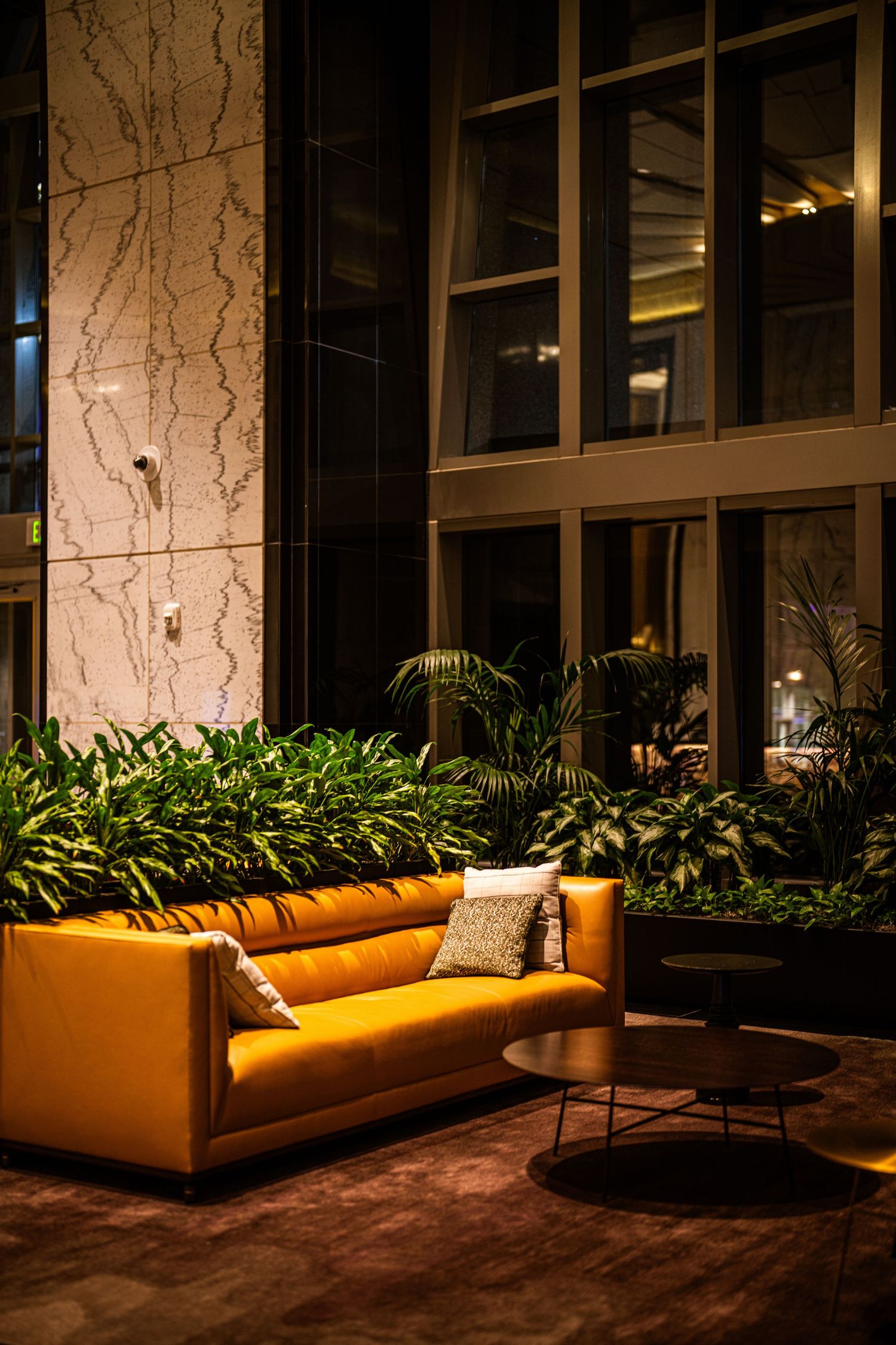 Modern lounge area with orange velvet sofa and indoor plants in an elegant lobby setting.