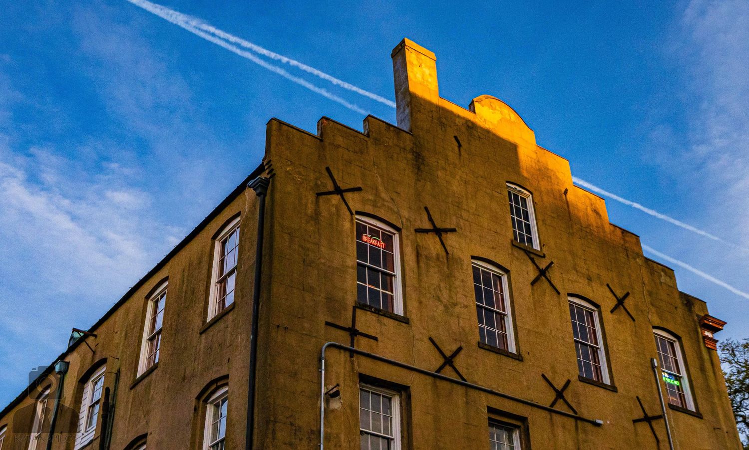 Historic brick building with arched windows and blue sky with contrails visible above in Savannah, Georgia.