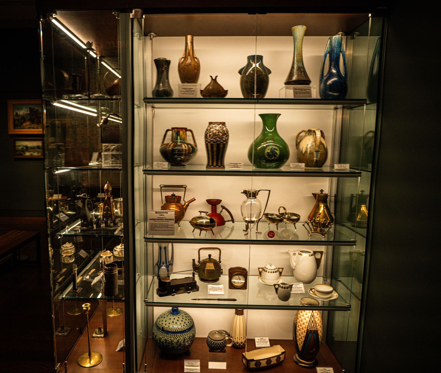A glass display case showcases a collection of vintage vases, bottles and decorative glassware on illuminated shelves.