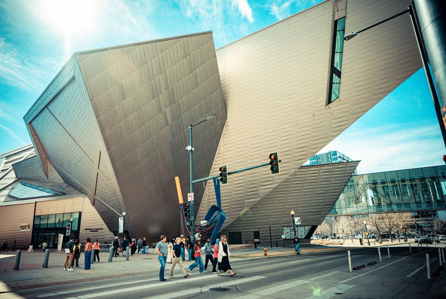 The angular architecture of the Denver Art Museum's Frederic C. Hamilton Building rises dramatically against a bright blue sky.