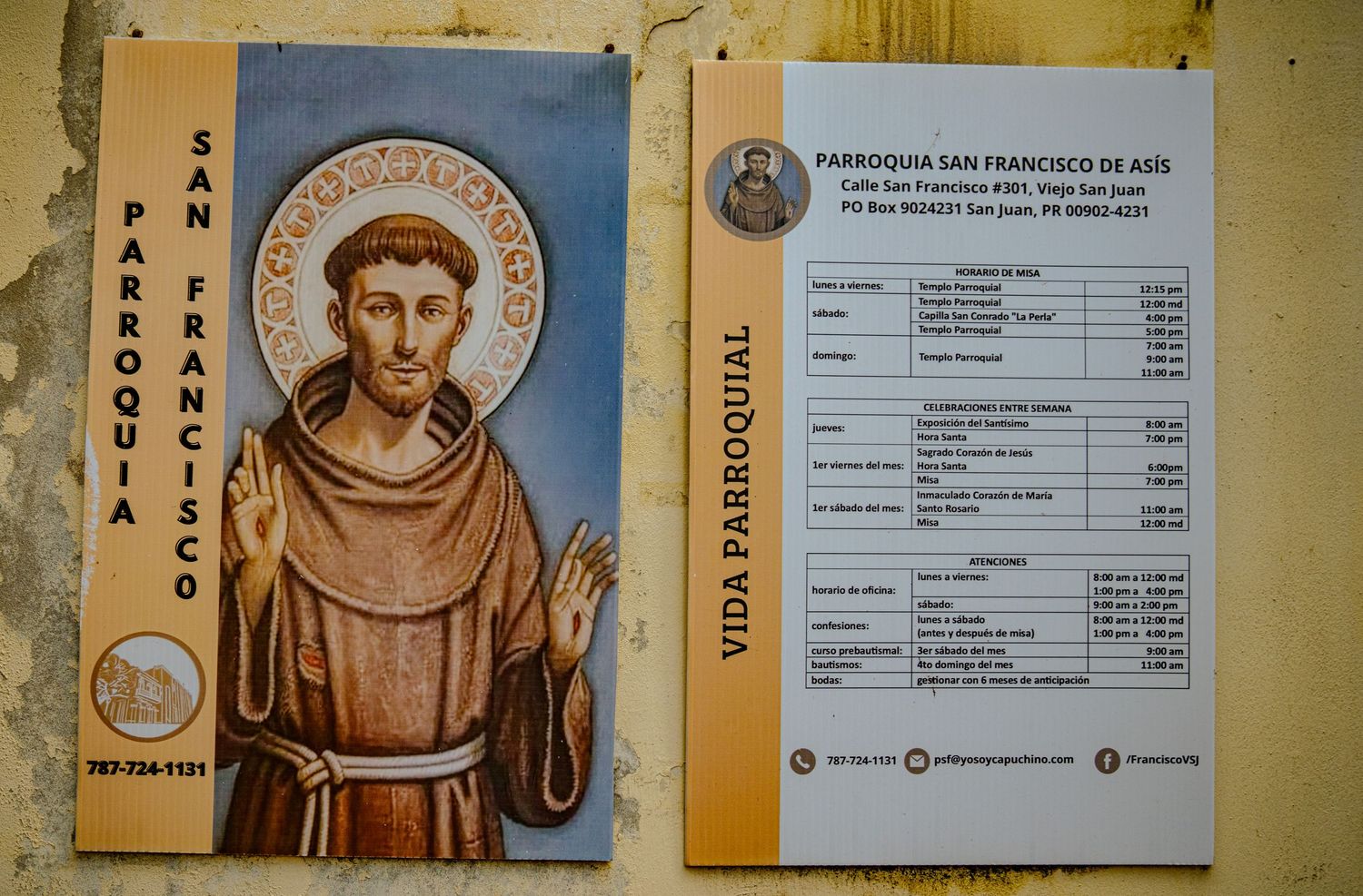 Religious artwork and informational signs displayed on a yellow wall showing schedule details and saint imagery.