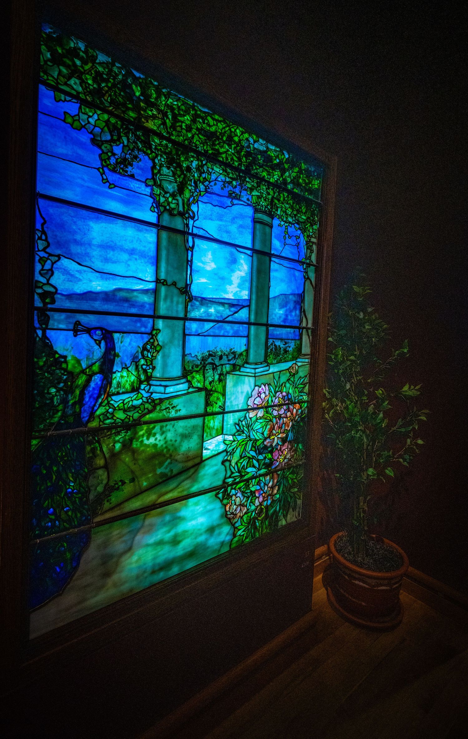 Stained glass window with blue sky and green vines creating a garden scene with dramatic lighting.