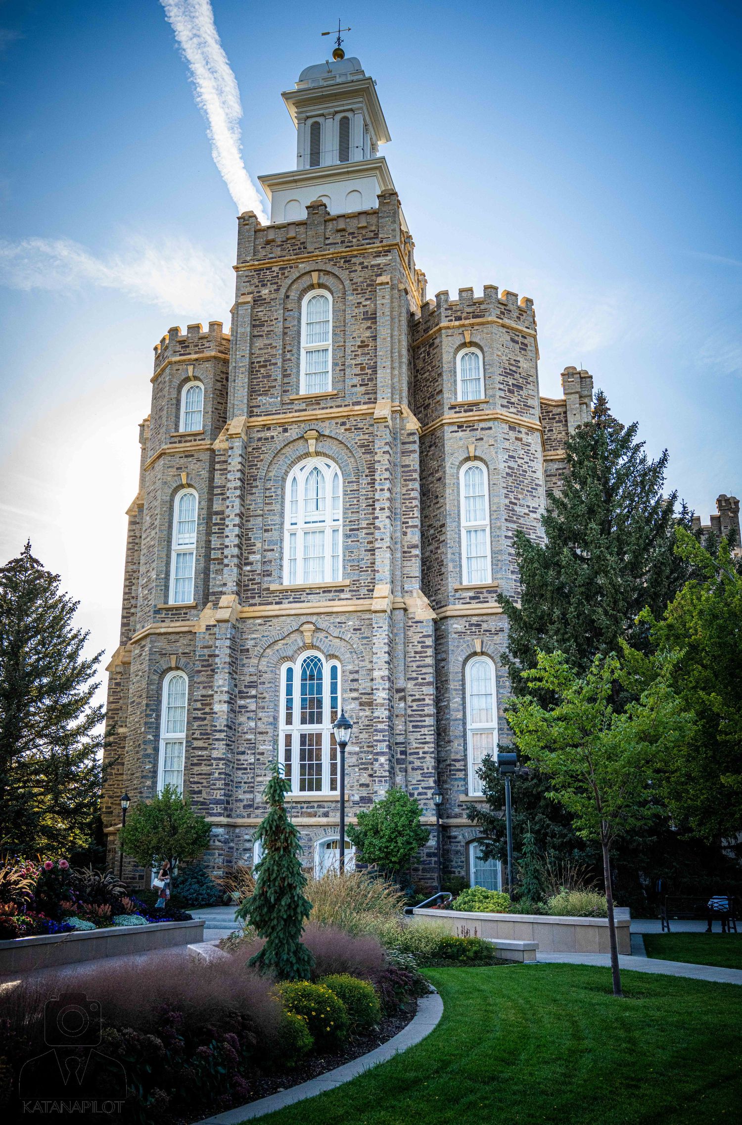 Gothic stone temple with tall arched windows and crenellated towers rises against a bright blue sky.
