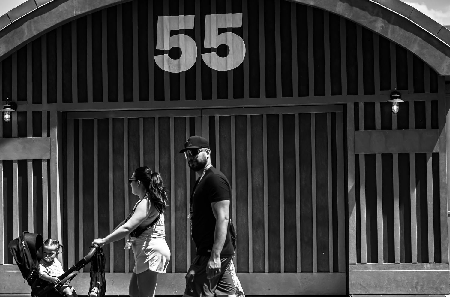 A black and white photograph shows people walking past a building marked with the number 55.