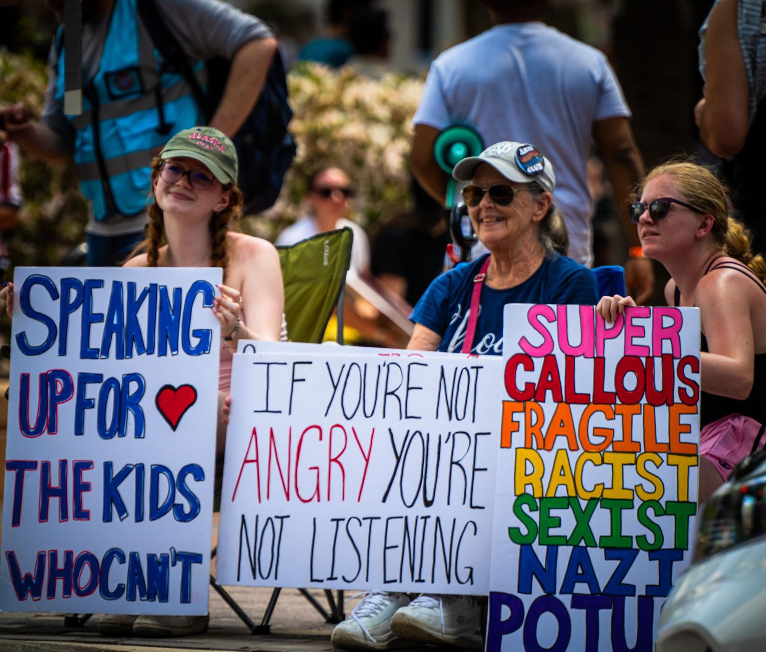 Protest signs being held up at a rally with messages about racism, speaking up, and listening to children's voices.