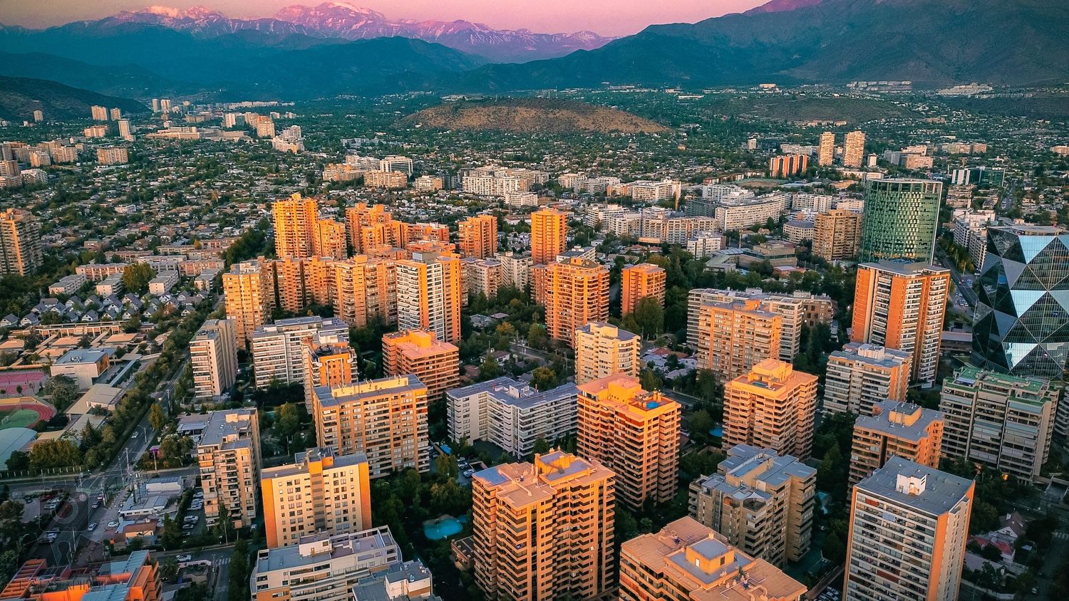 Urban skyline with high-rise buildings against mountain backdrop at dusk.