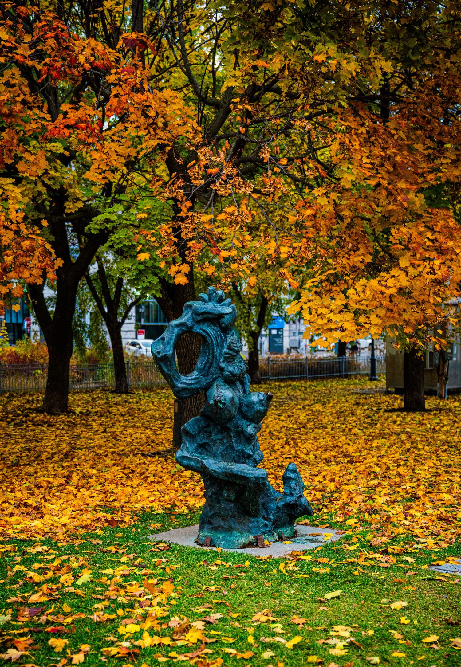 Bronze statue in a park surrounded by autumn trees with vibrant orange and yellow leaves covering the ground.