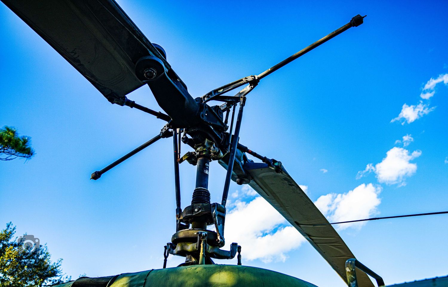 Helicopter rotor blades and mechanical components photographed against bright blue sky.