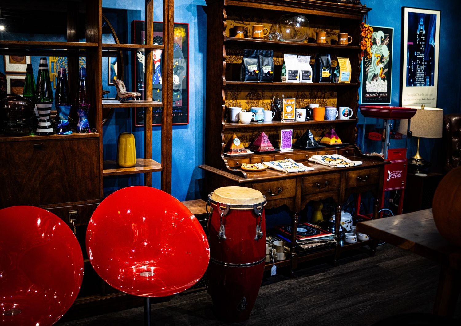 Row of red bar stools line up along a dark wooden bar counter in a moody blue-lit establishment.