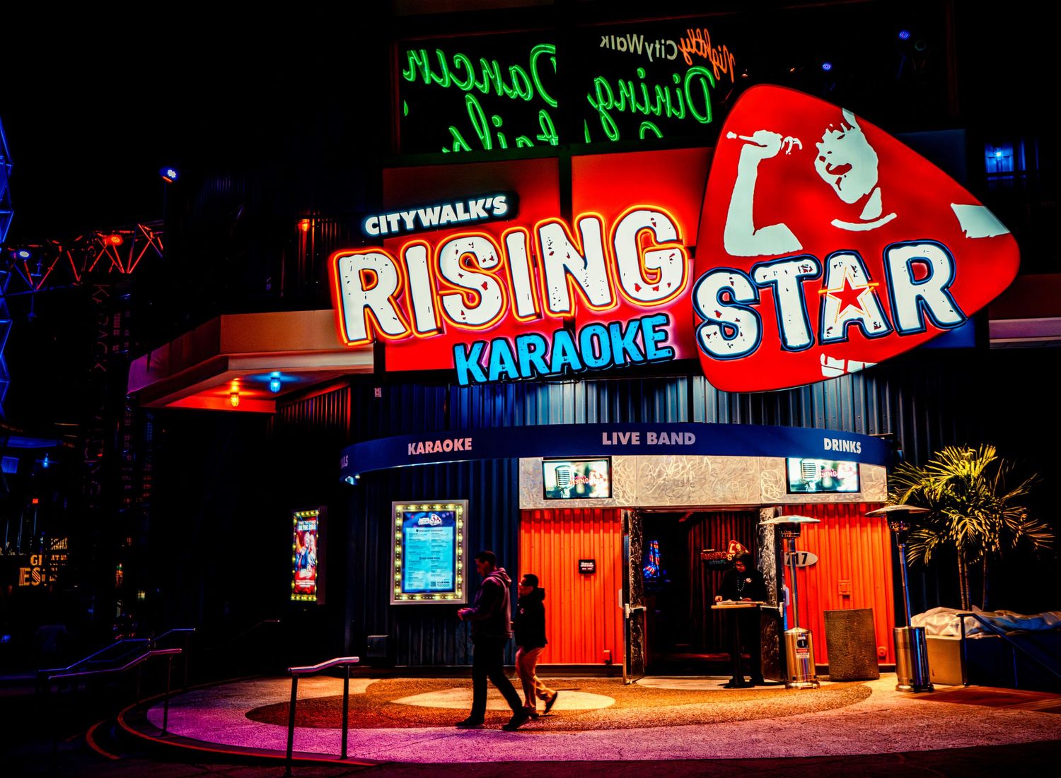 Colorful neon signs illuminate multiple storefronts and businesses at night creating a vibrant urban scene.