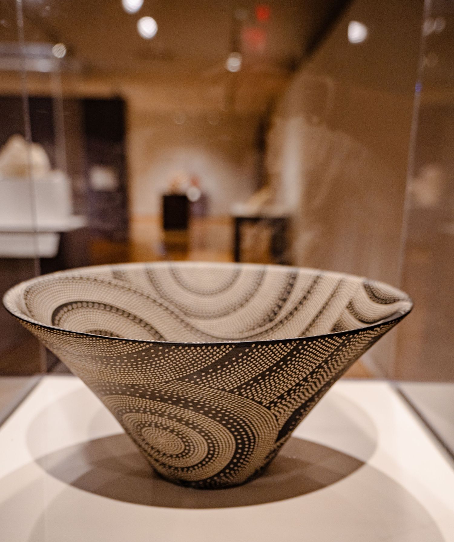 Intricately patterned black and white ceramic bowl with swirling dot designs displayed in a museum glass case.