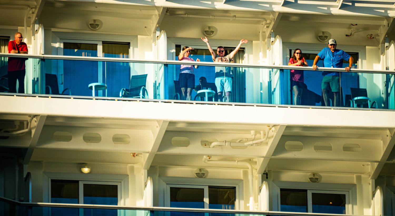 A row of white cruise ship balconies with blue railings against a bright sky on a sunny day.