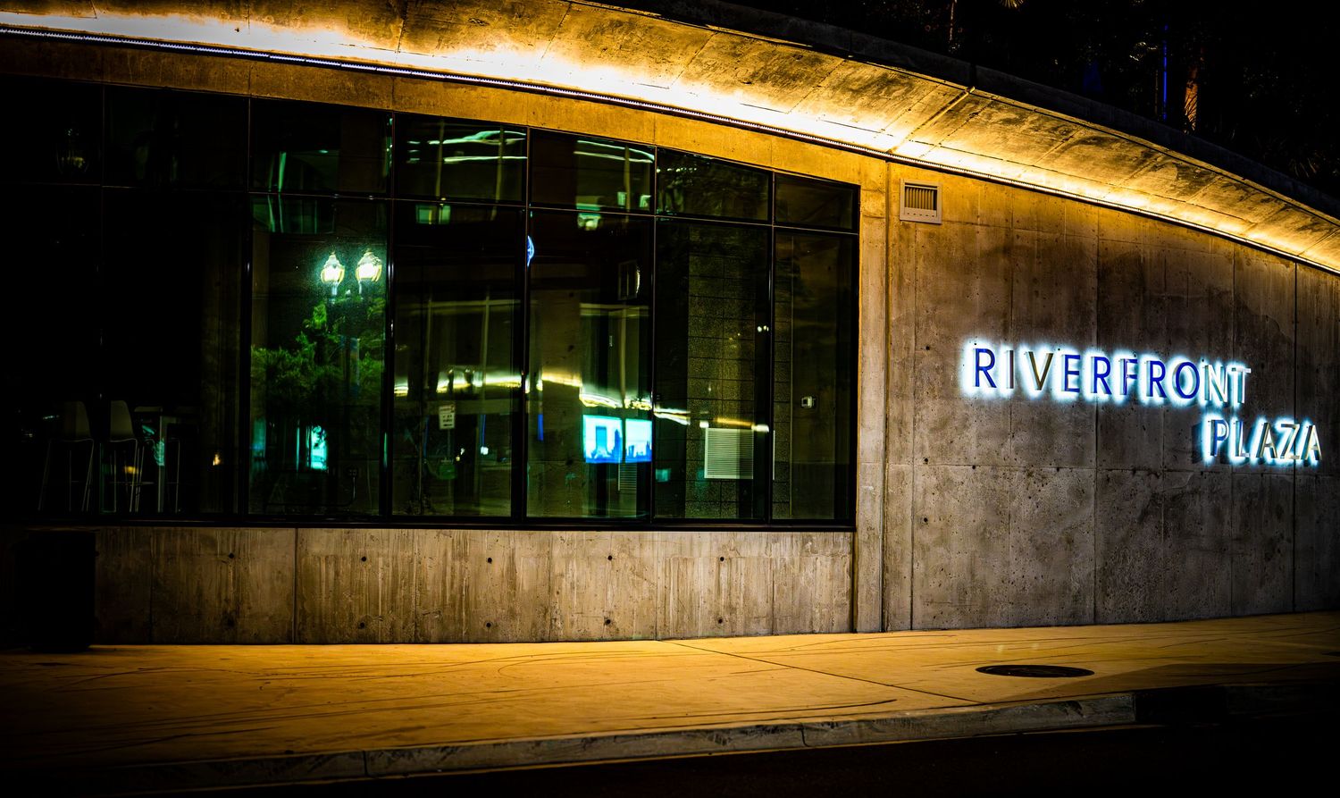 Riverfront Plaza illuminated sign glowing in blue neon light on modern building exterior at night.