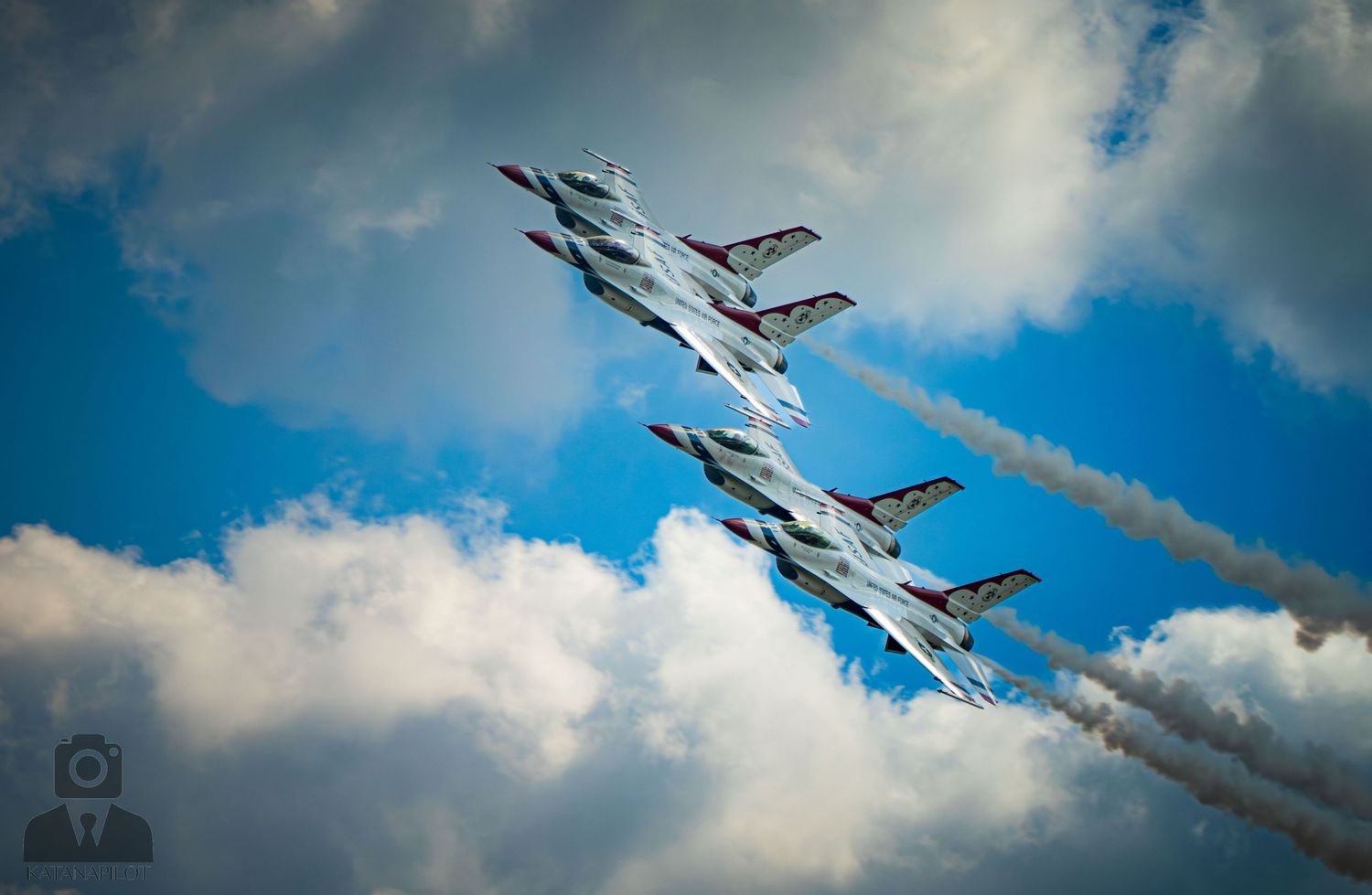Four military jets perform a dramatic aerial formation with smoke trails against a blue cloudy sky.