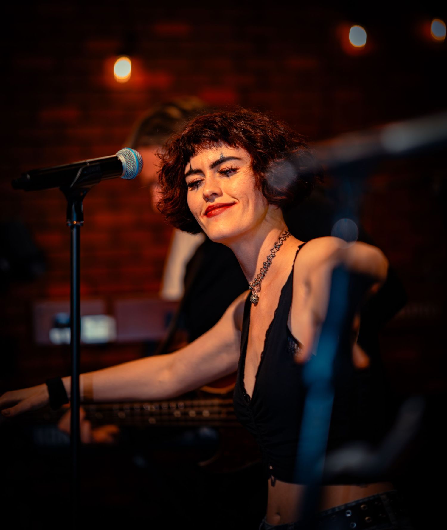 Singer performs at microphone against red brick wall with mood lighting.