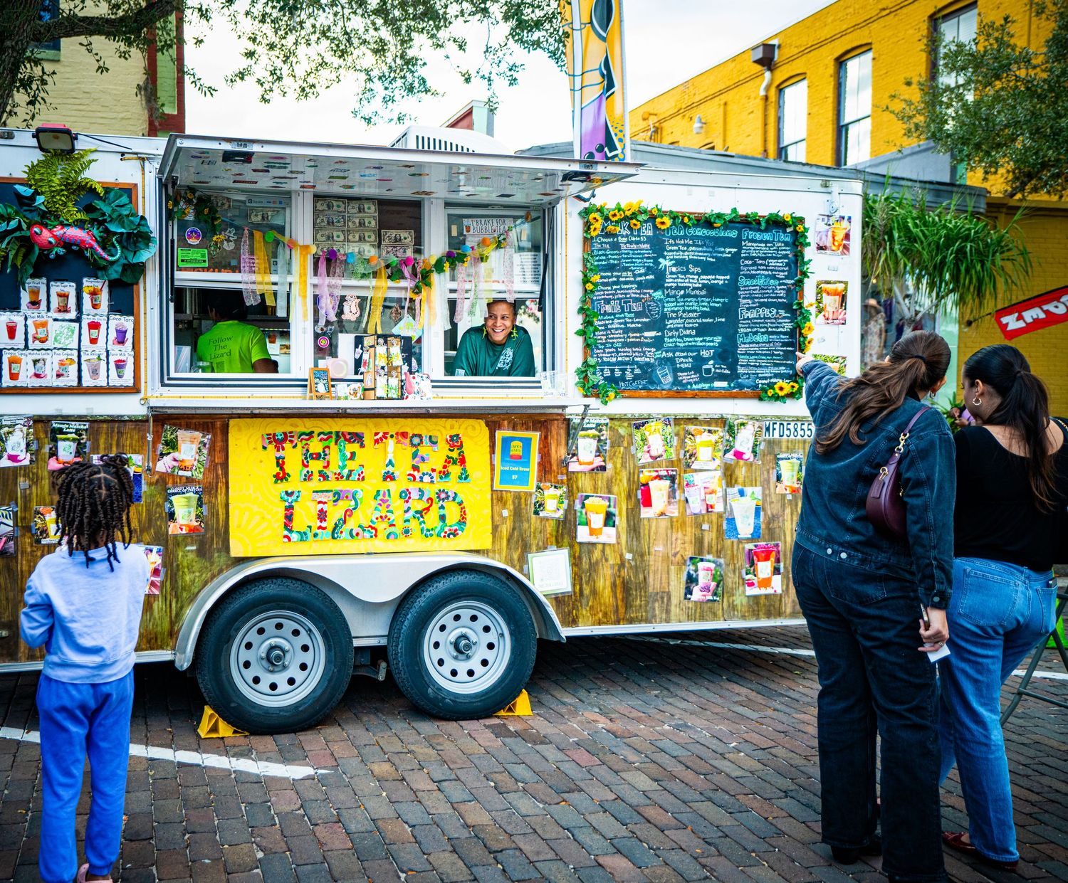 Colorful food trucks and vendor stalls line a brick walkway at an outdoor food court area.
